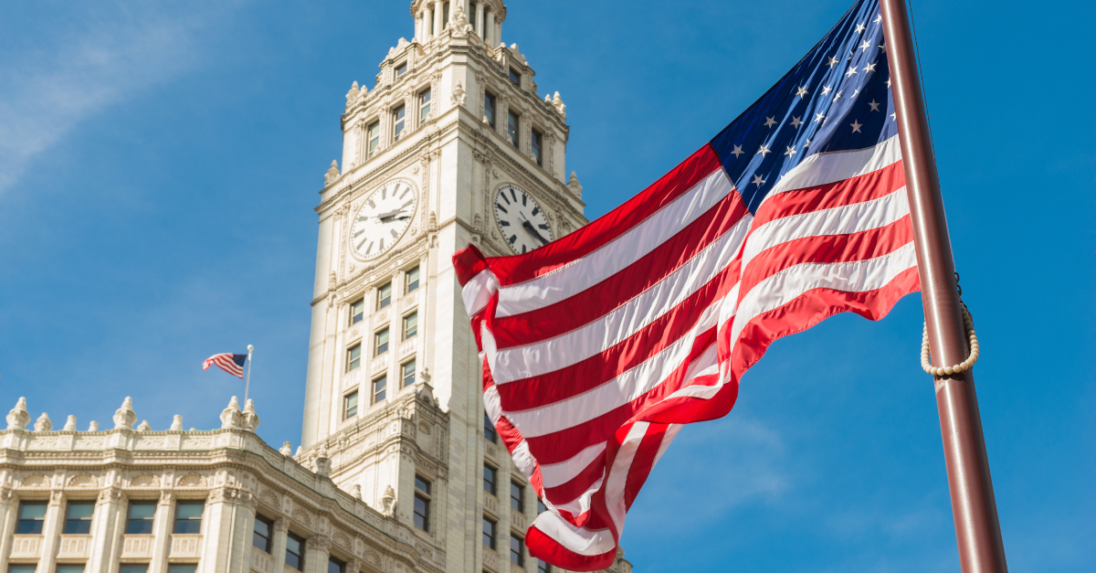 A picture of the US flag in the foreground, on a backdrop of a state building.