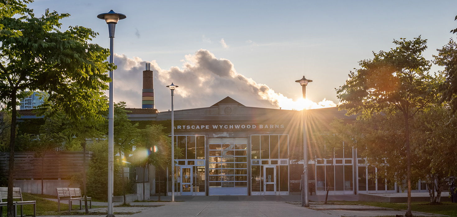 On a cloudy day, sun rays peek out from behind Artscape Wychwood Barns.