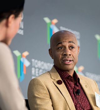 Black man in suit speaking during panel discussion.