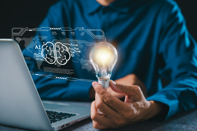 A person at a laptop holds a lightbulb