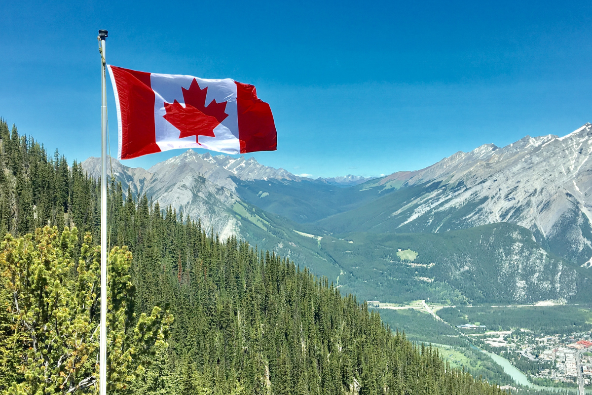 The Canadian flag in the foreground, set amidst a hilly, green backdrop.