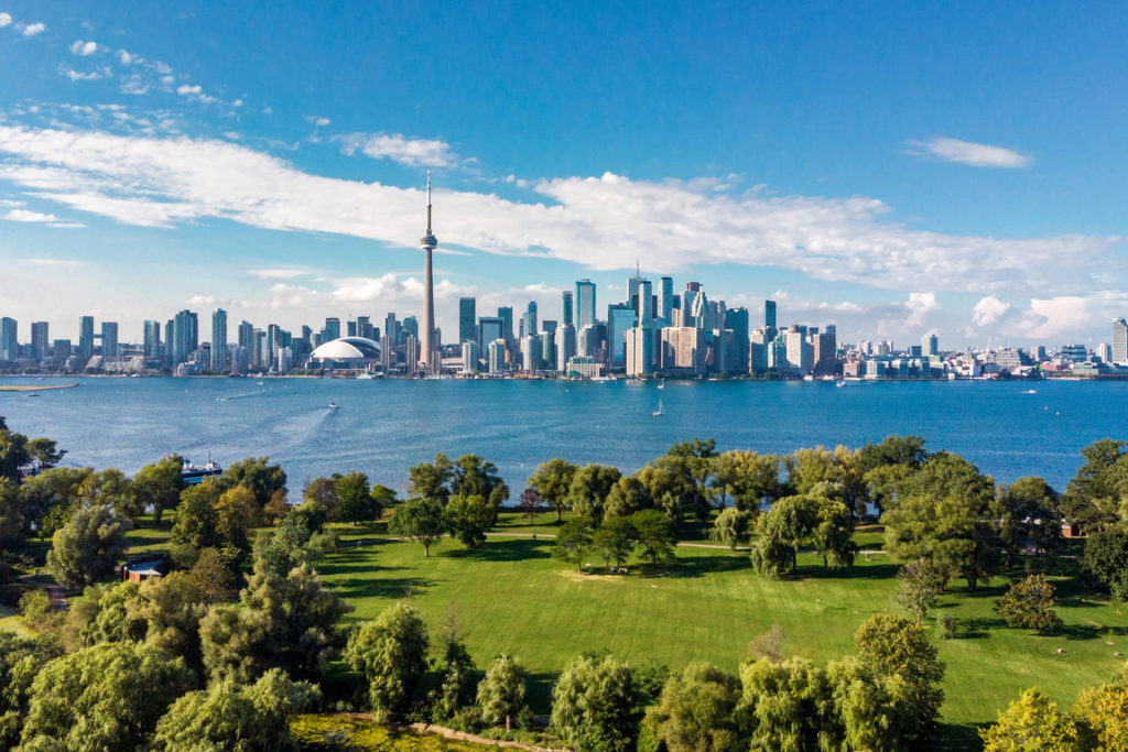 A view of Toronto from the other side of the lake, with green pastures in the foreground.